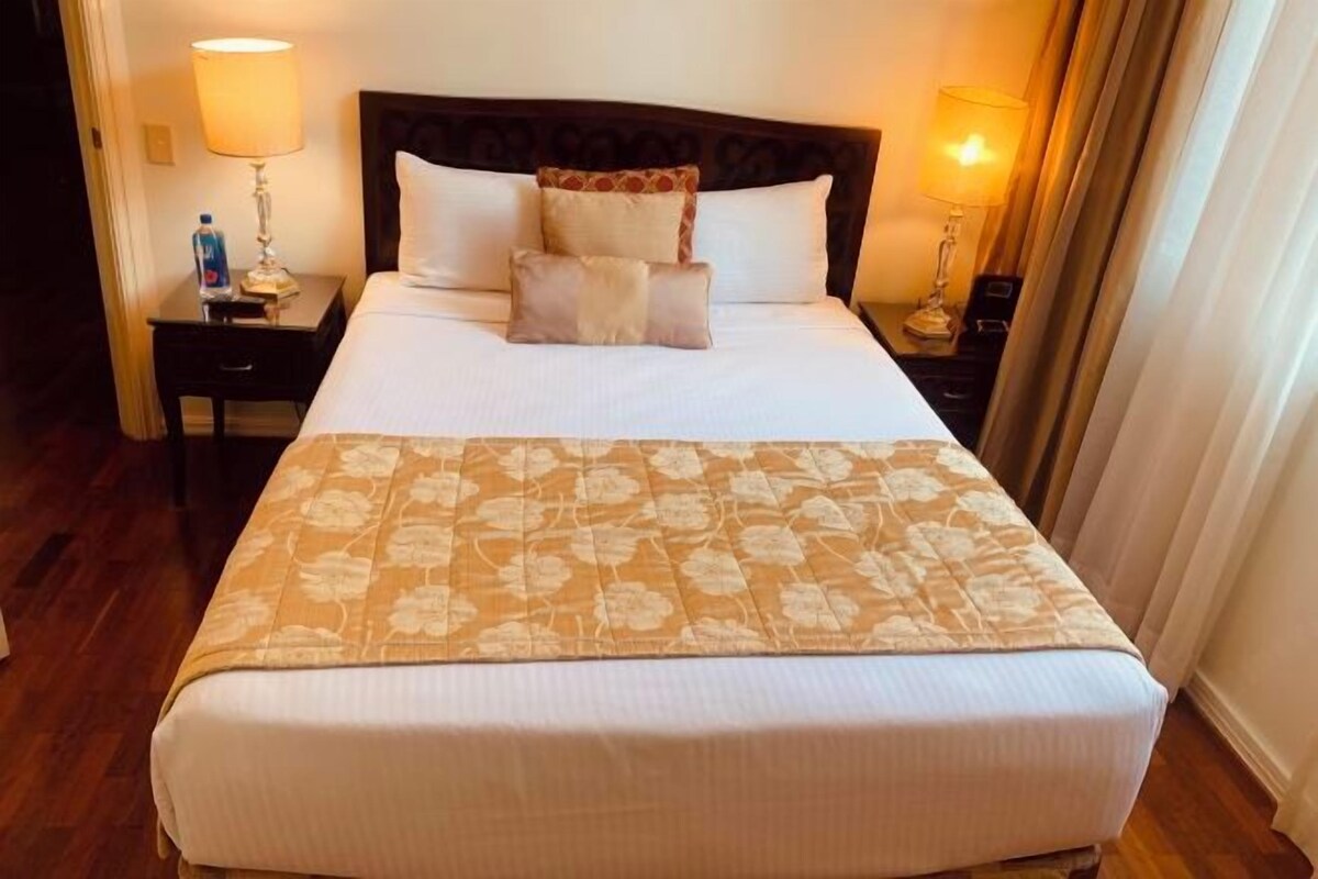 A hotel room with a large bed, two bedside tables, and lamps.