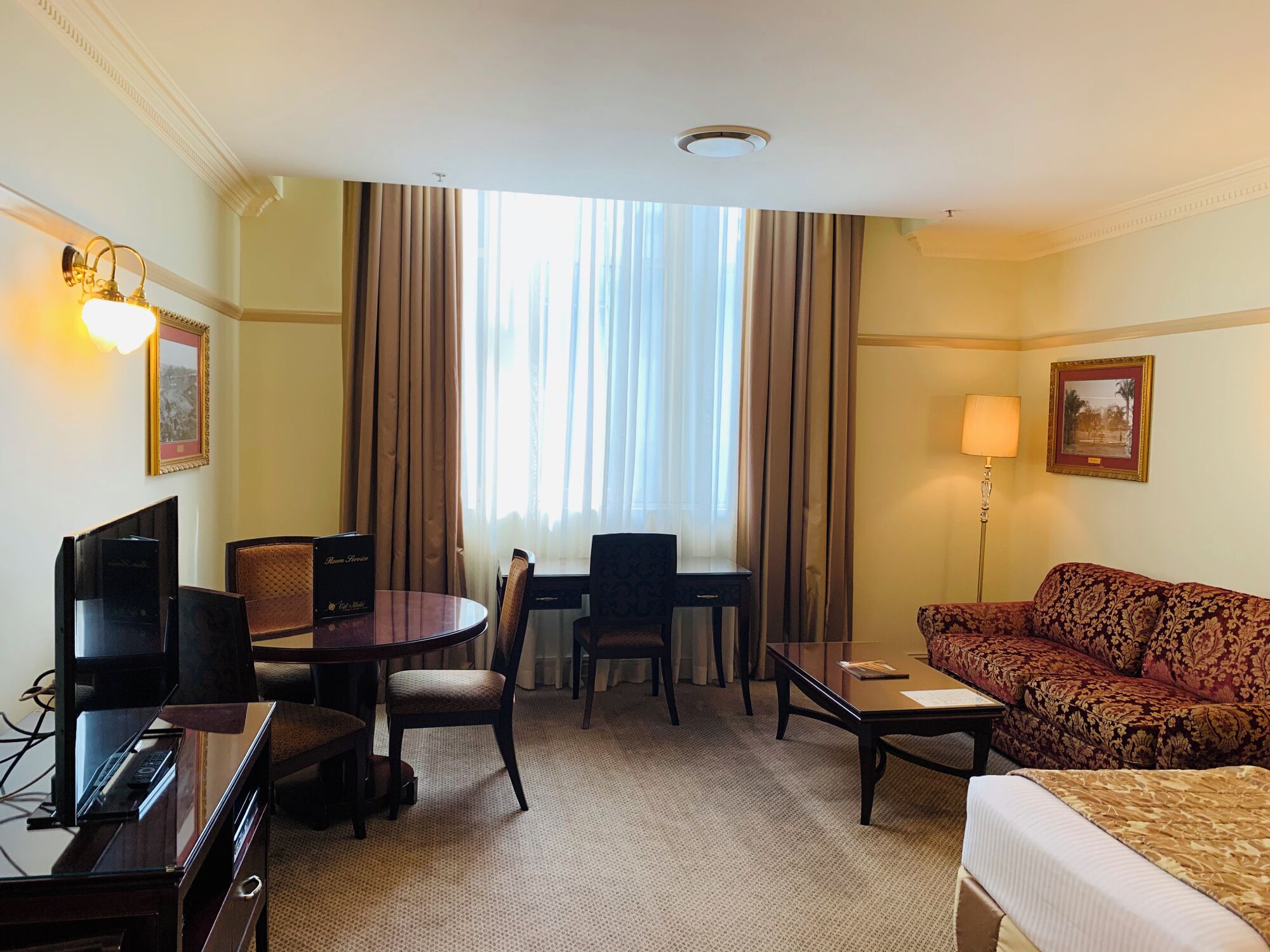 A hotel room with a bed, a sofa, a desk with a chair, a television, and a window with curtains.