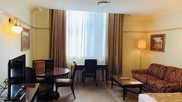 A hotel room with a bed, a sofa, a desk with a chair, a television, and a window with curtains.