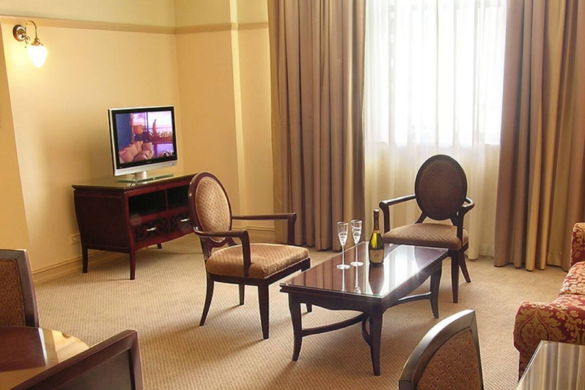 A hotel room with a television, a sofa, a dining table, and a chair.