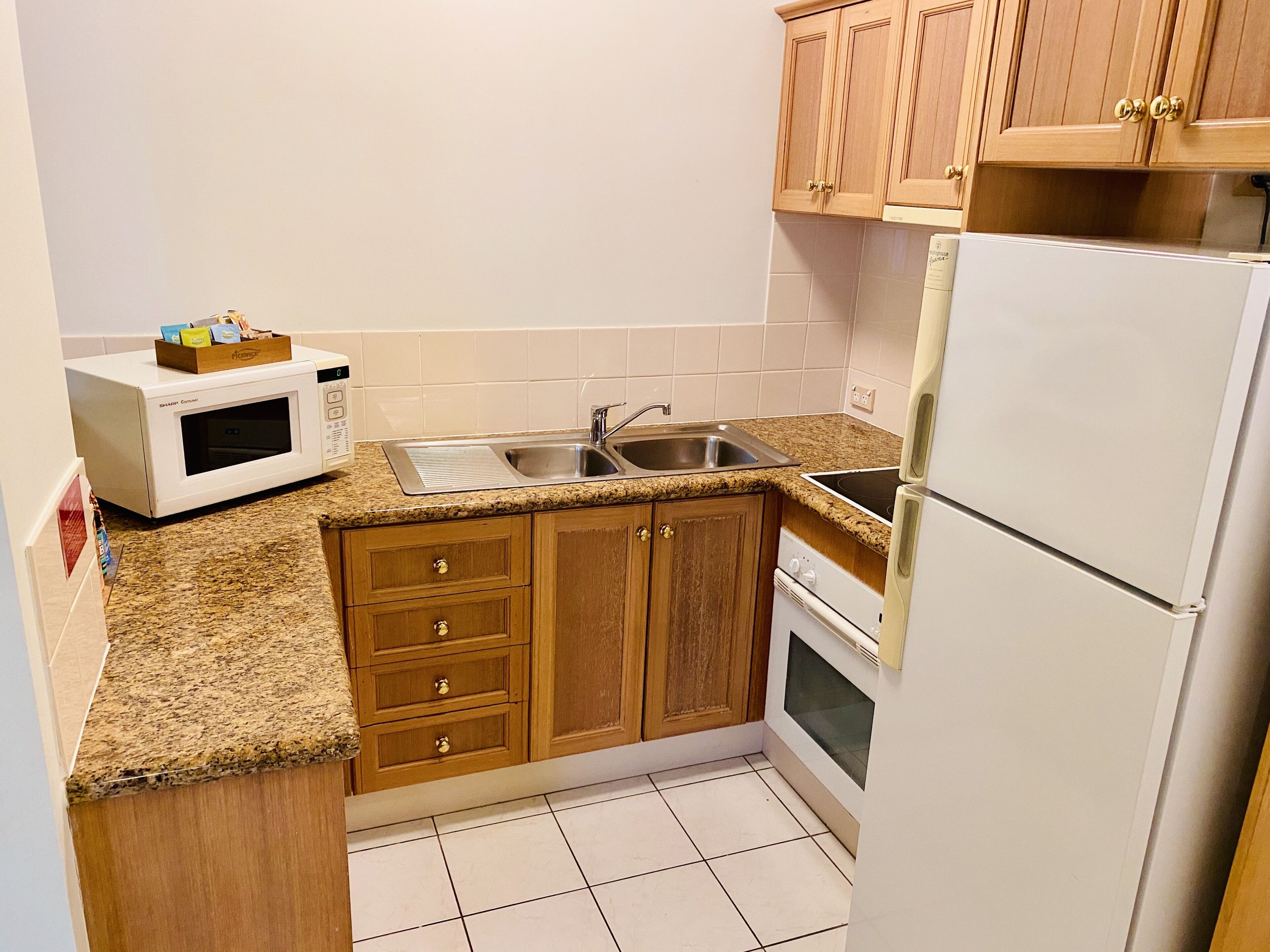 A compact kitchen with wooden cabinets, a built-in microwave, a sink, and a refrigerator.