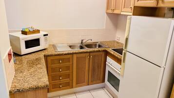 A compact kitchen with wooden cabinets, a built-in microwave, a sink, and a refrigerator.