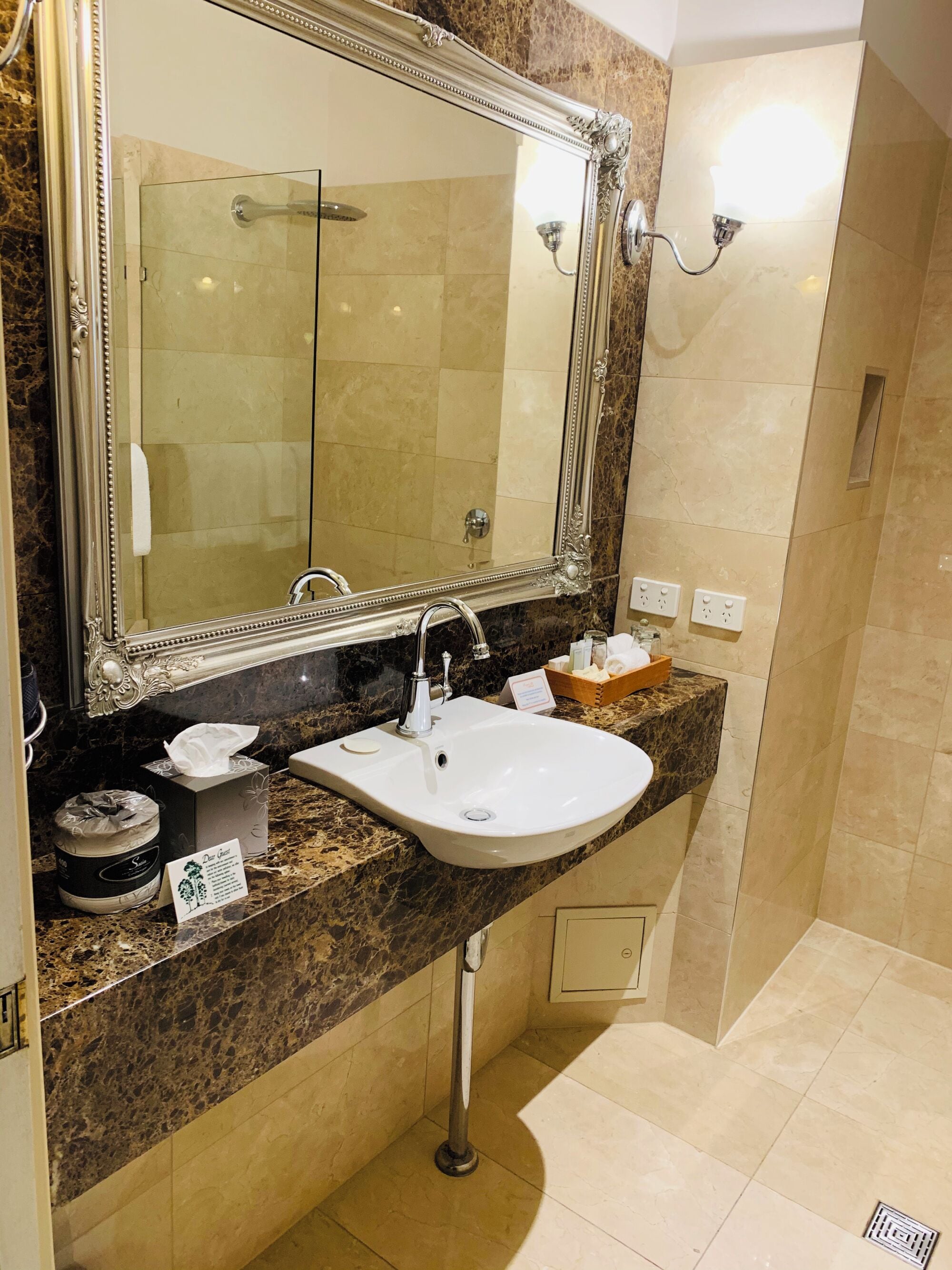 Un baño con un espejo grande, lavabo, ducha y encimera de mármol.