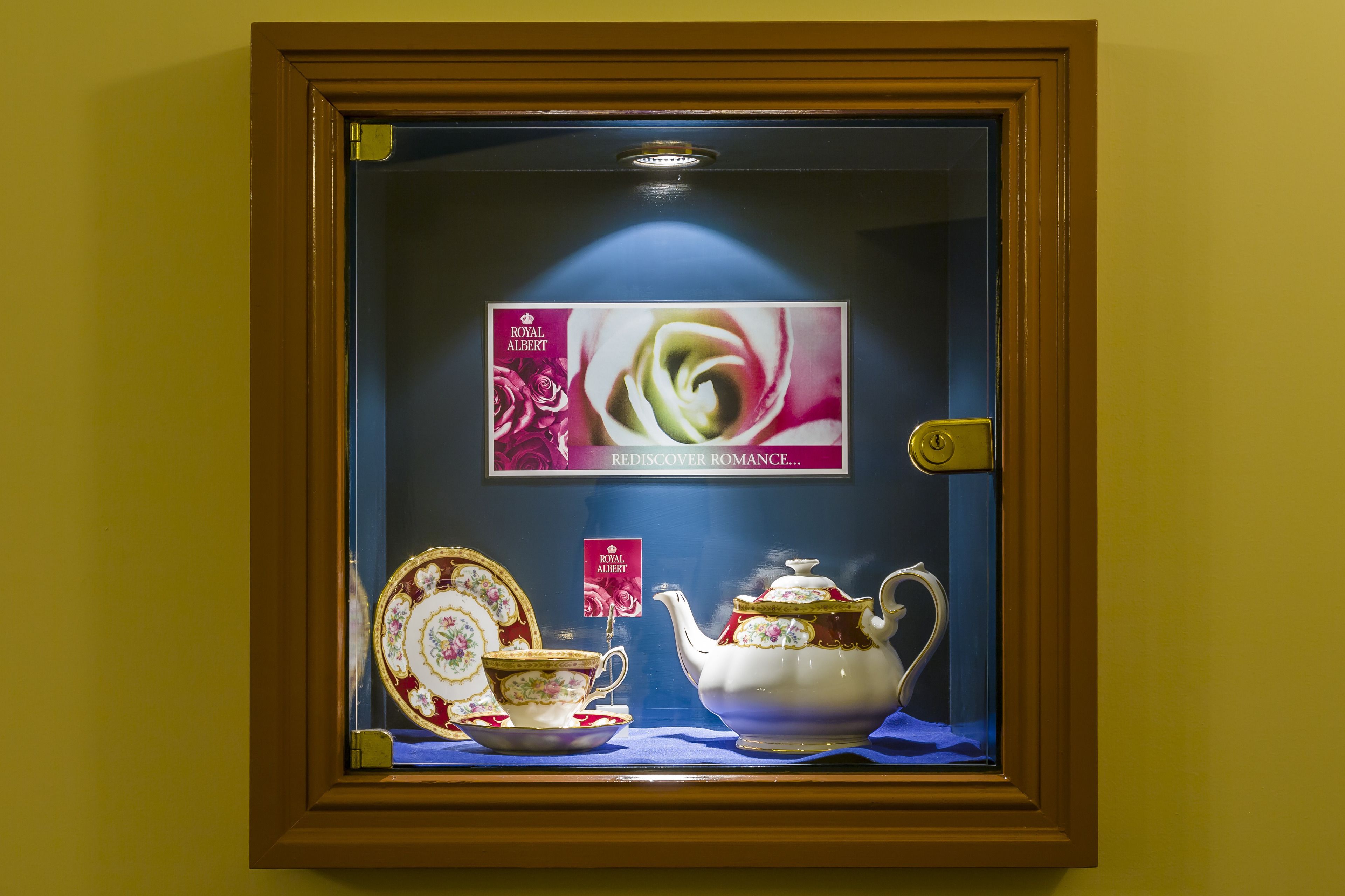 A framed display of Royal Albert tea set with a sign reading "Rediscover Romance...".