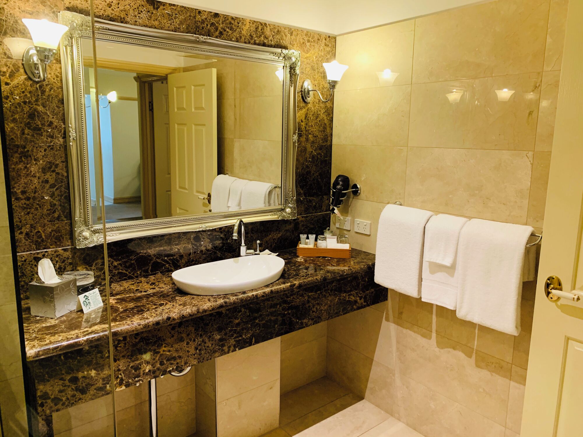 A bathroom with a marble countertop, a sink, a large mirror, and a towel rack.