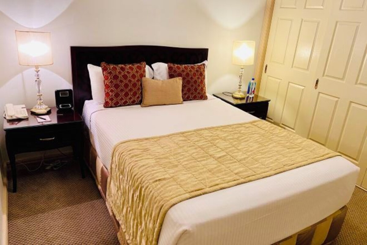 A hotel room with a large bed, two bedside tables, a nightstand, a lamp, a phone, and a door.