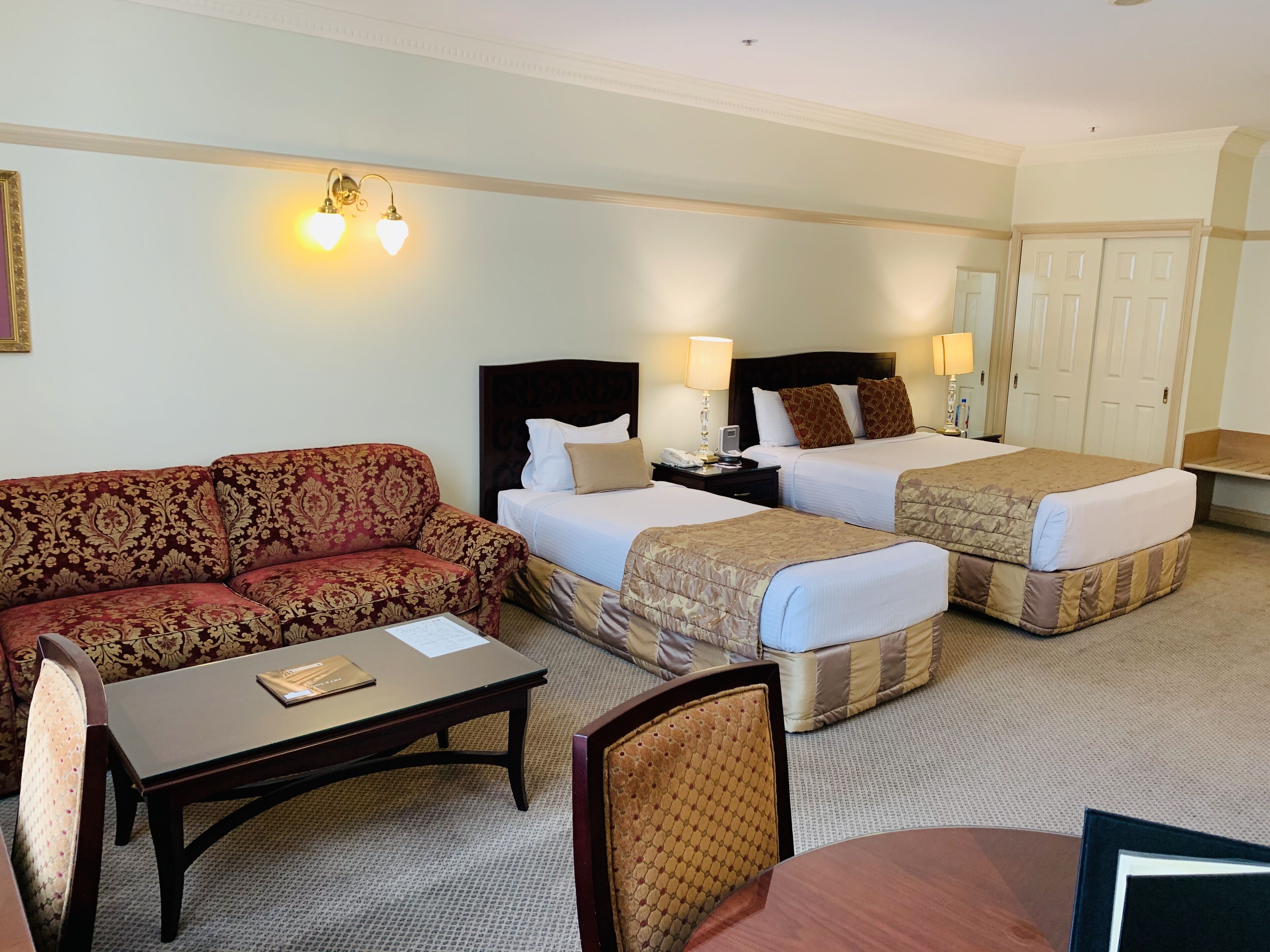 A hotel room with a sofa, two single beds, a desk, and a chair.
