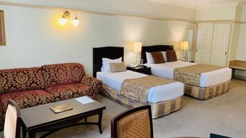 A hotel room with a sofa, two single beds, a desk, and a chair.