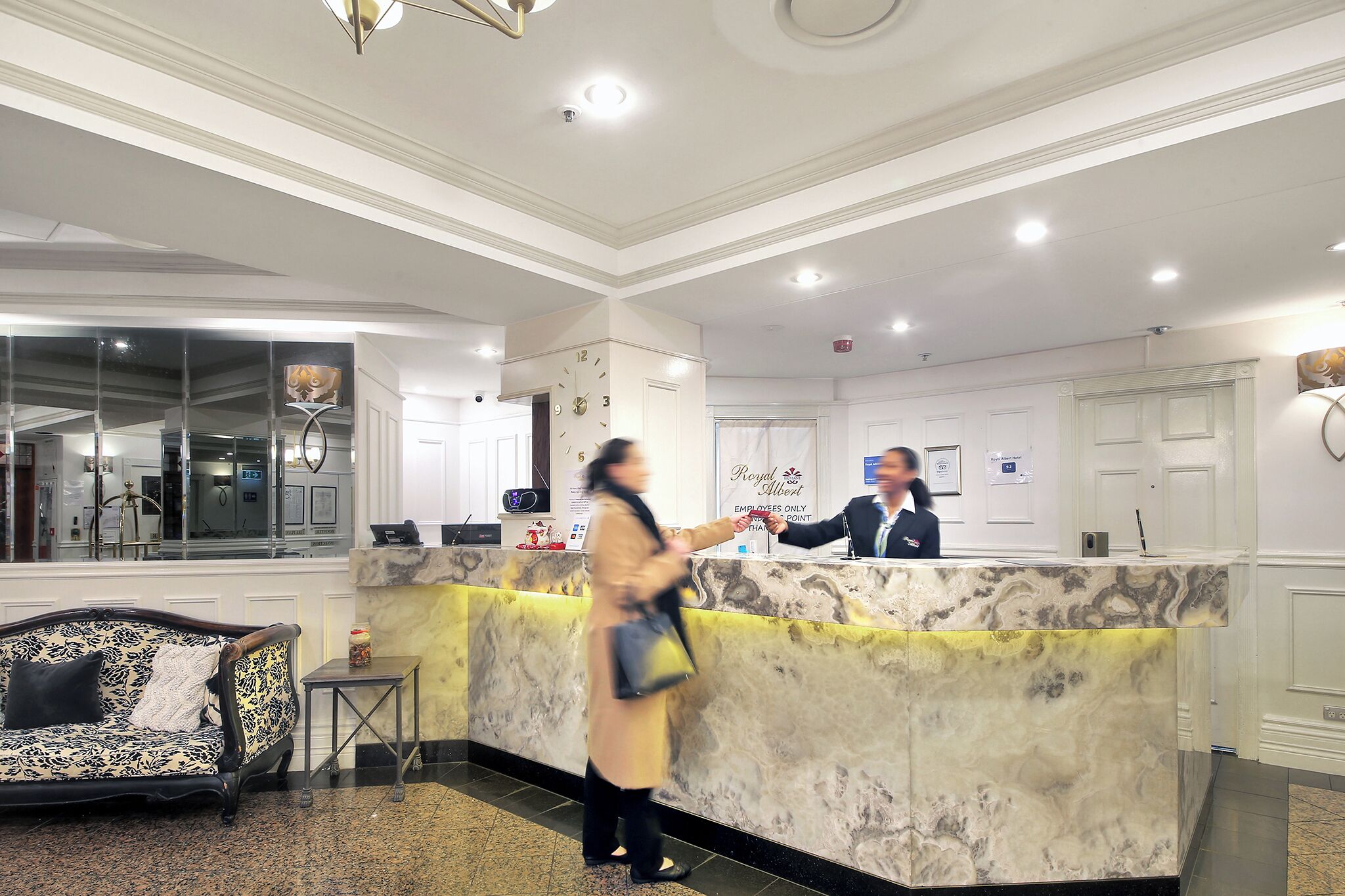A hotel reception area with a marble counter, a sofa, and a clock on the wall.