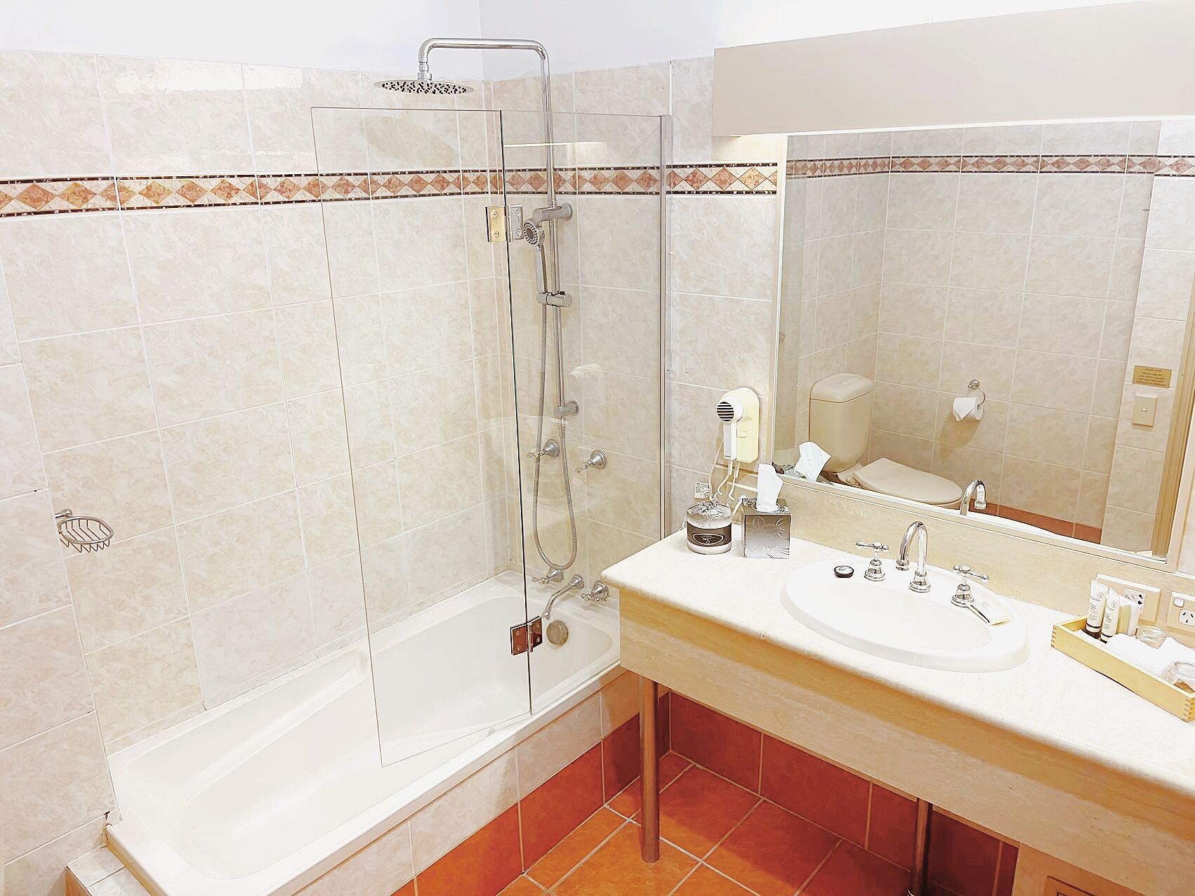 Ein Badezimmer mit einer gläsernen Duschkabine, einem Waschbecken mit Spiegel und einer Toilette.