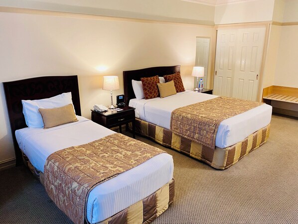 A hotel room with two beds, each with a headboard, bedside tables with lamps, and a carpeted floor.