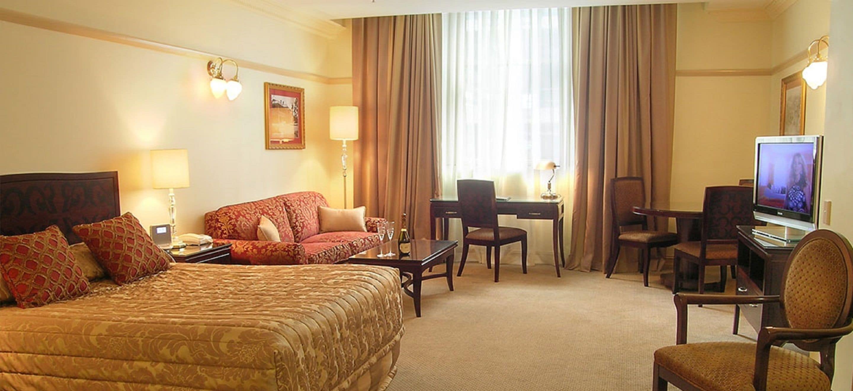 A hotel room with a large bed, a desk with a chair, a television, and a window with curtains.