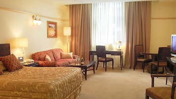 A hotel room with a large bed, a desk with a chair, a television, and a window with curtains.