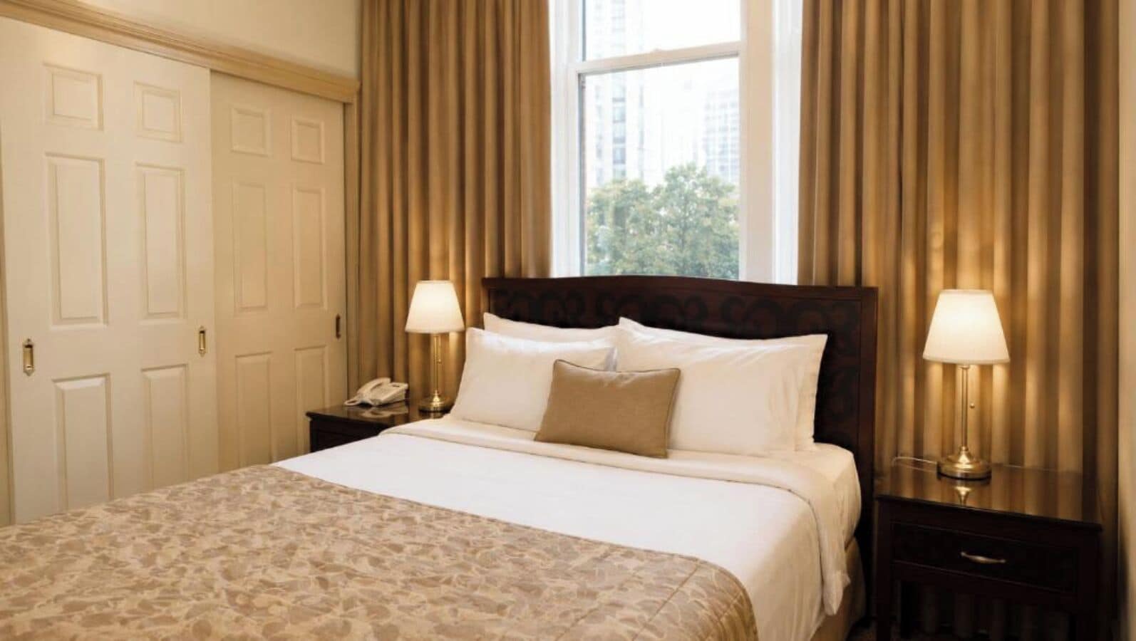 Habitación de hotel con una cama grande, dos lámparas de noche, una mesita de noche con teléfono y una ventana con cortinas.