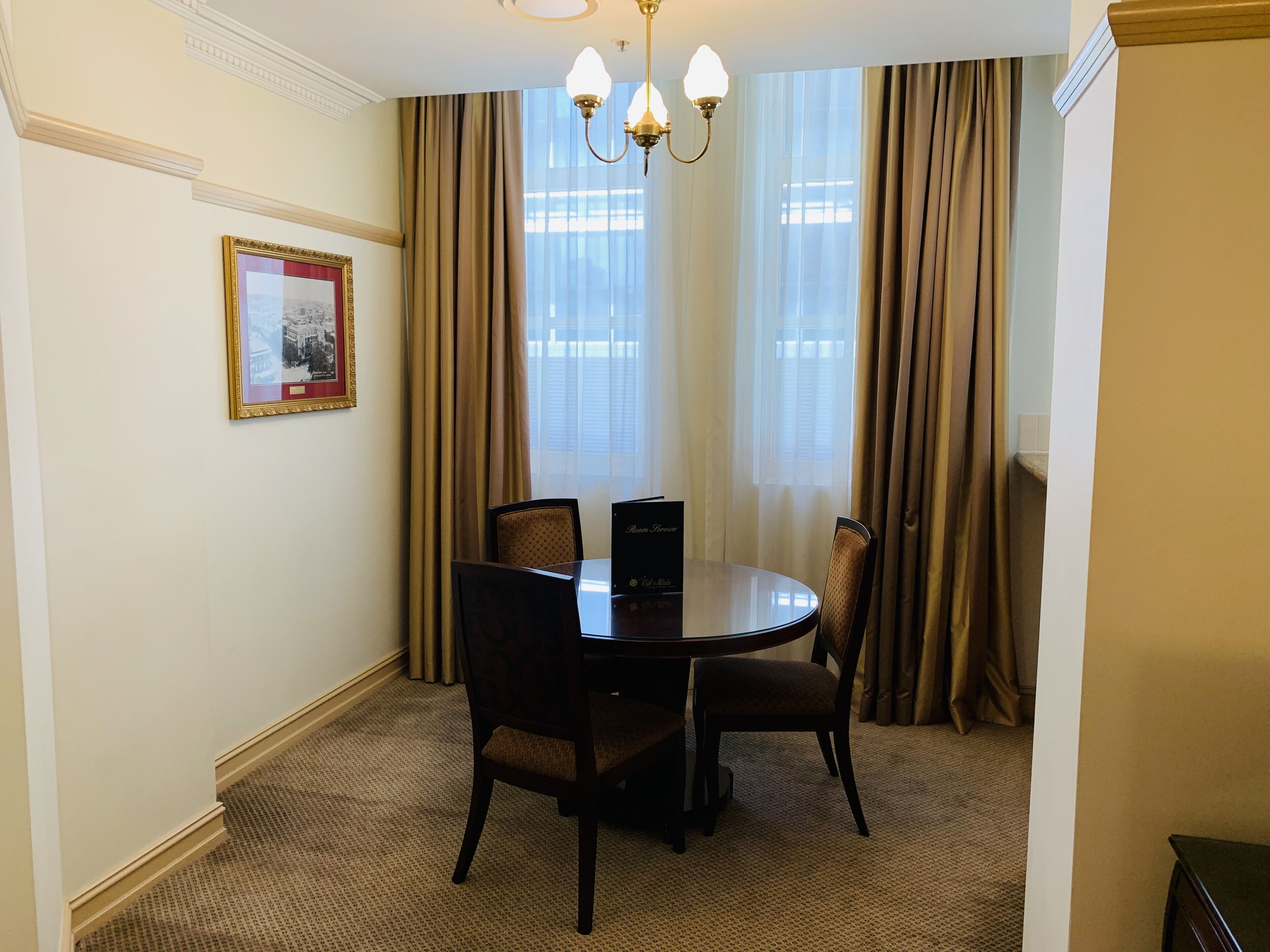 Un coin repas avec une table ronde, quatre chaises, un lustre et un tableau encadré au mur.