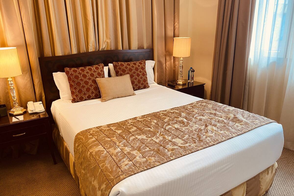 A hotel room with a large bed, two bedside tables, a lamp, a phone, and a notebook on one table.