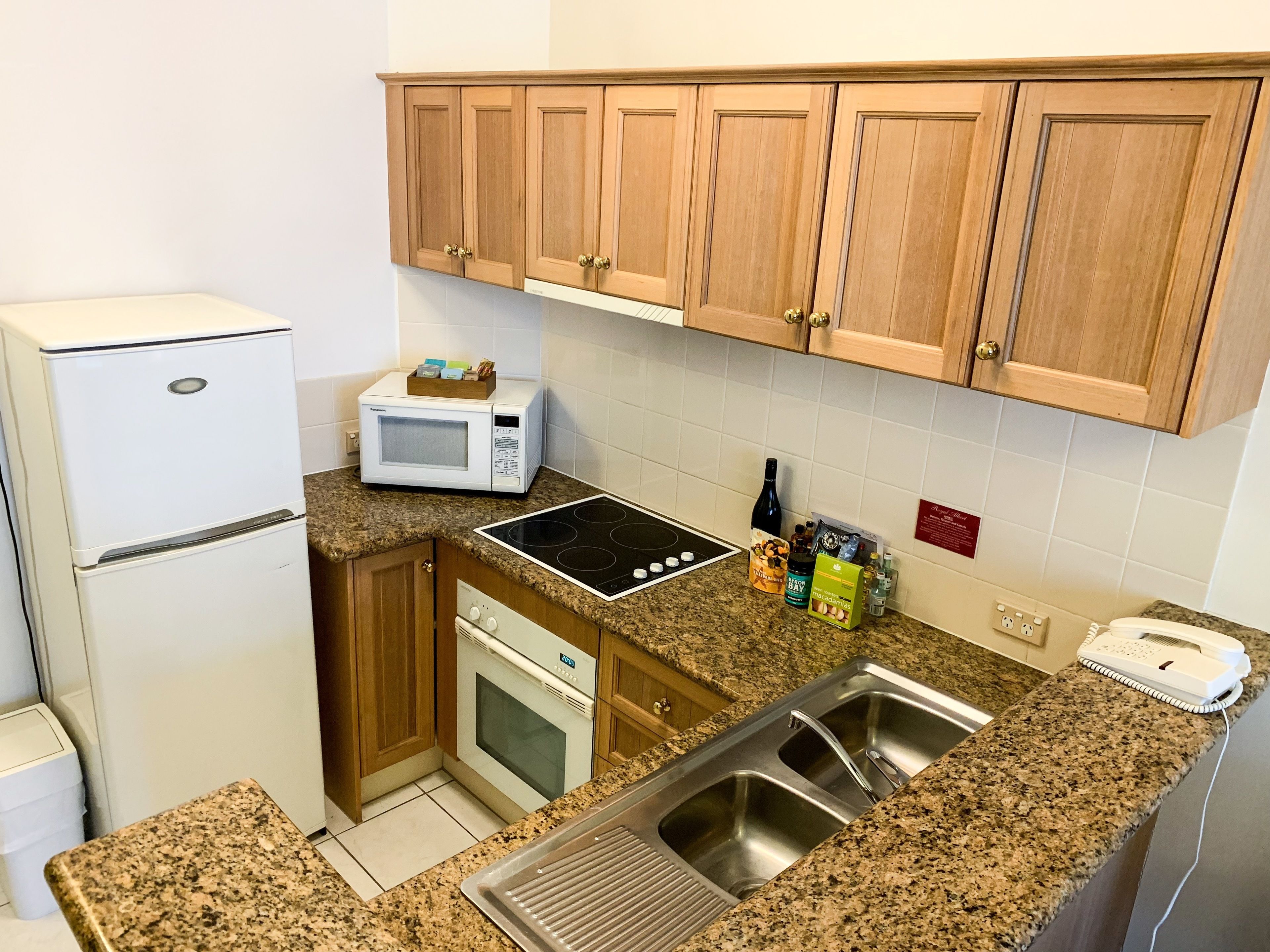 A compact kitchen with a refrigerator, microwave, stove, sink, and wooden cabinets.
