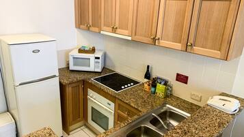 A compact kitchen with a refrigerator, microwave, stove, sink, and wooden cabinets.