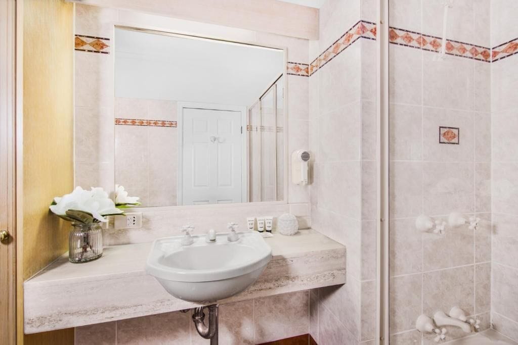 A bathroom with a sink, mirror, and shower.
