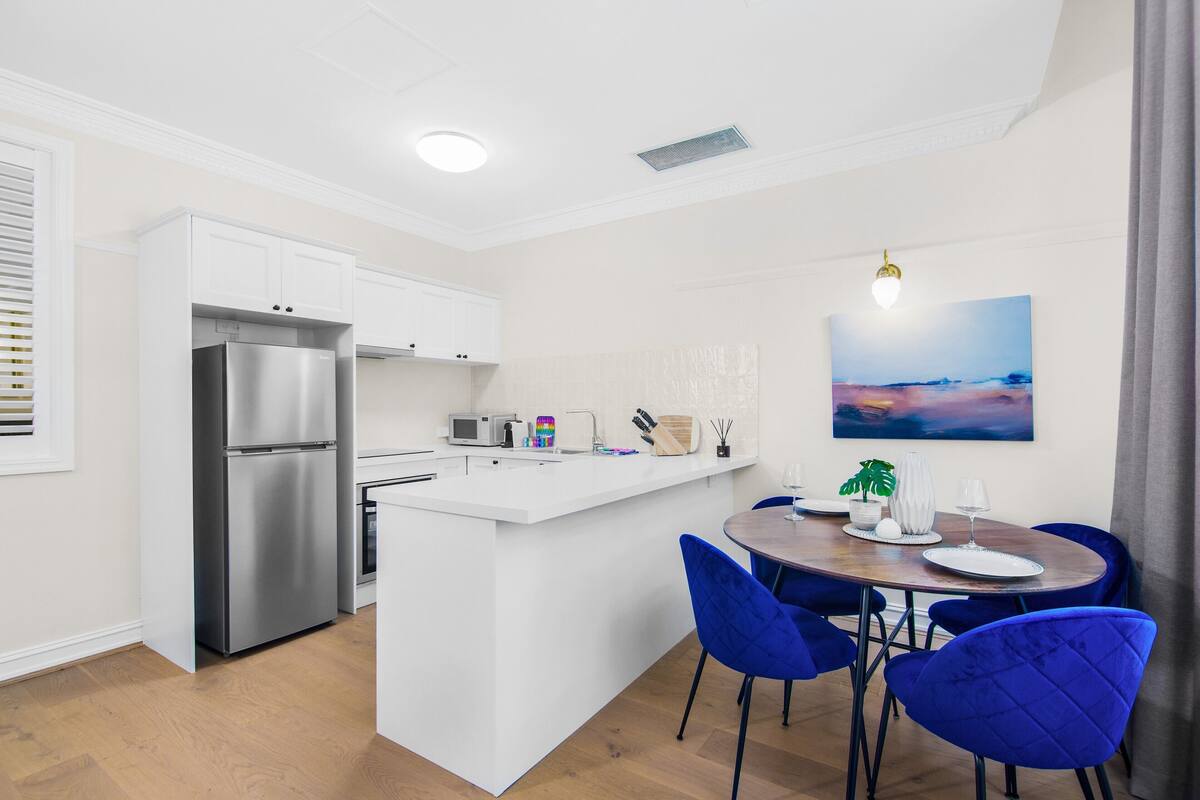 A modern kitchen with white cabinetry, a stainless steel refrigerator, and a central island with seating.