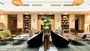 A spacious lobby with a high ceiling, a central seating area with sofas and chairs, and a large bookshelf filled with books. - Renaissance Paris Vendome Hotel (Paris)