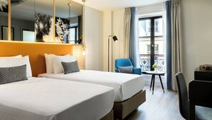 A hotel room with two beds, a large mirror, a desk with a chair, a small table, and a balcony with curtains. - Renaissance Paris Vendome Hotel (Paris)