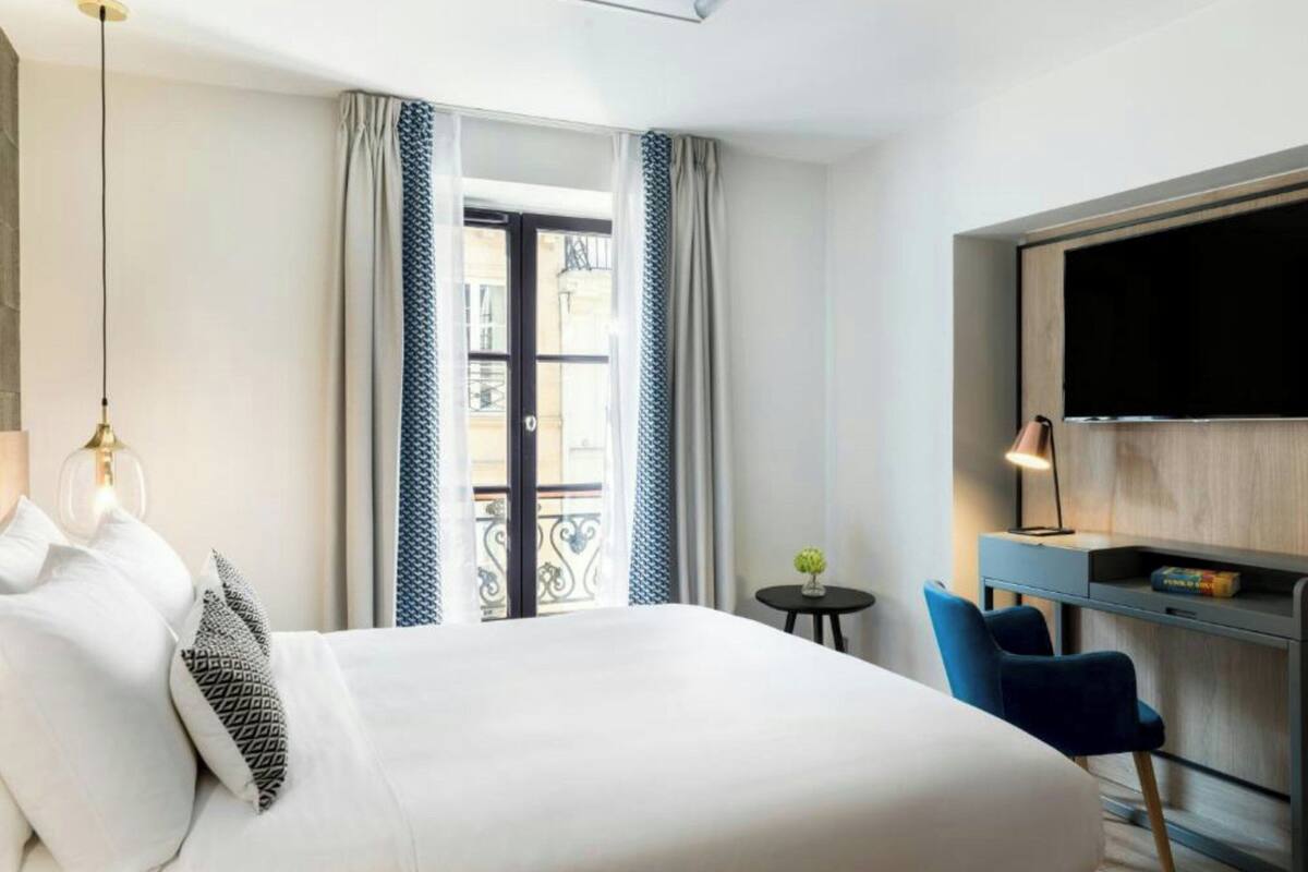 A hotel room with a large bed, a desk with a chair, a TV, and a small table with a lamp.
