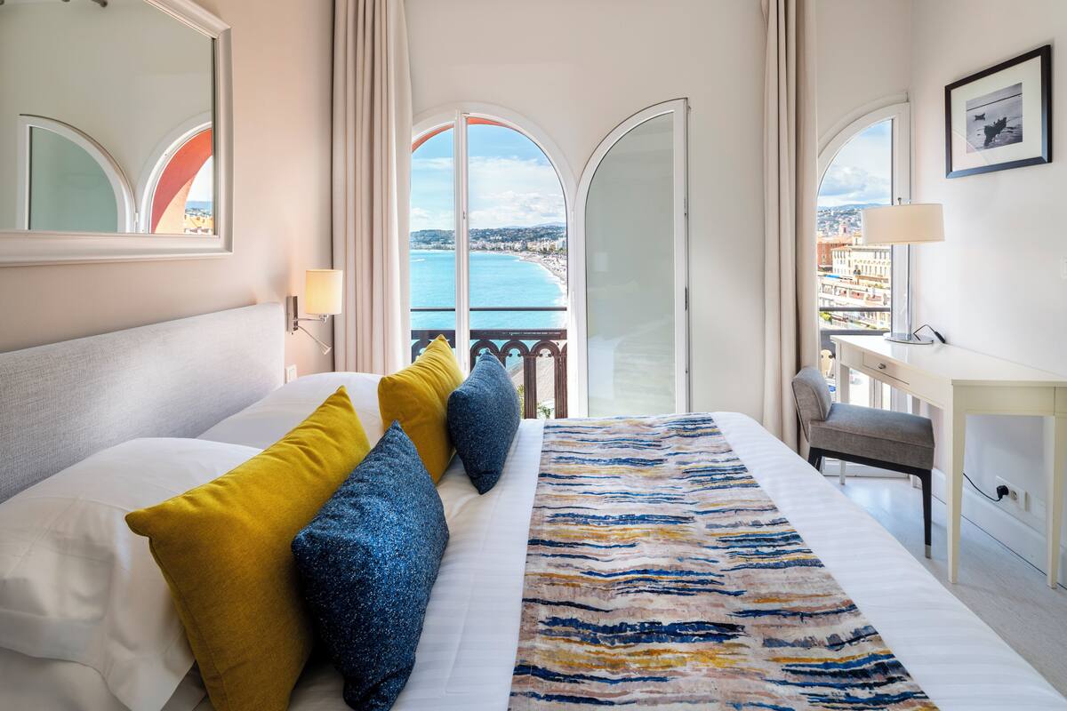A hotel room with a bed, a desk, and a view of the sea.