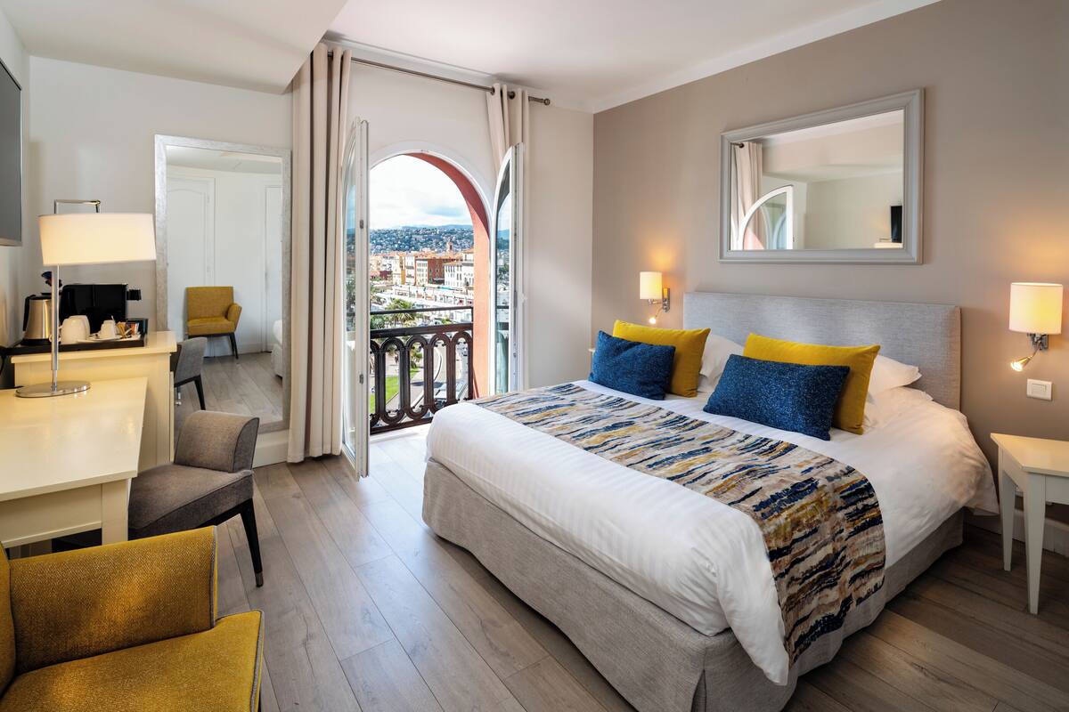 A hotel room with a bed, a desk, a chair, and a balcony with a city view.