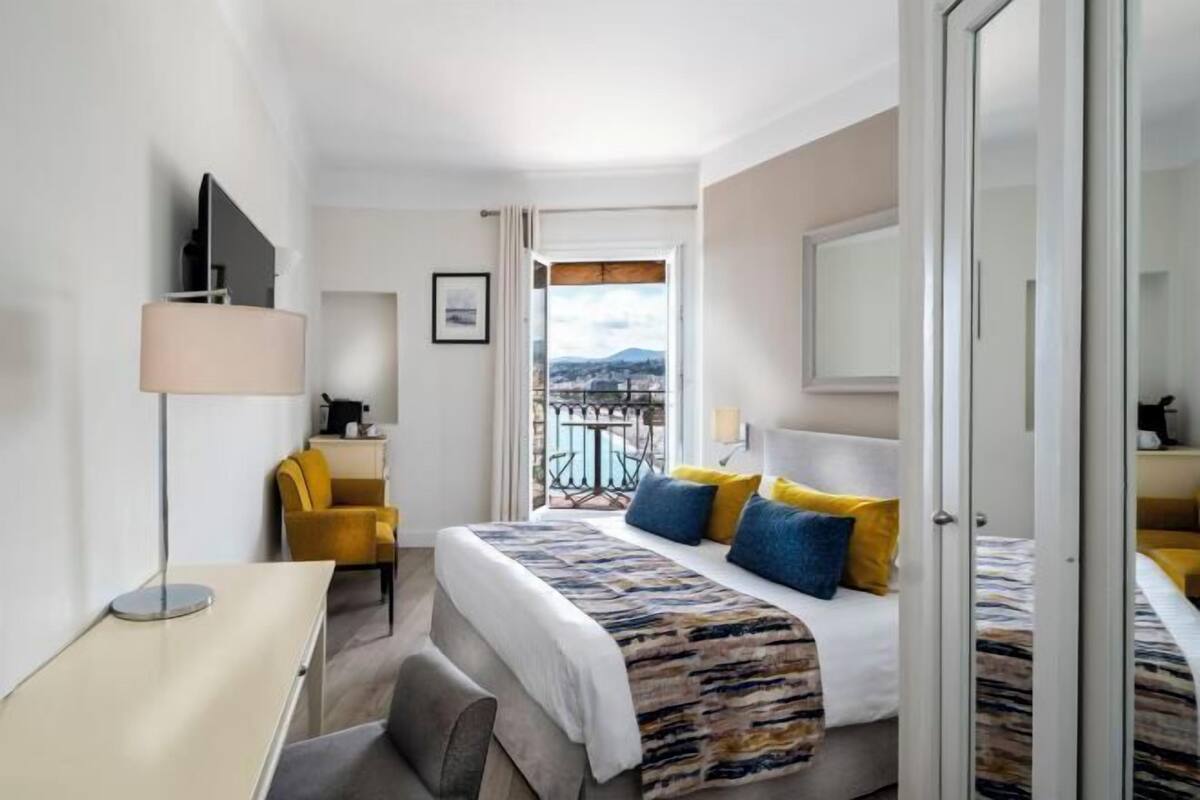 A hotel room with a bed, a desk, a chair, a TV, and a balcony with a view.