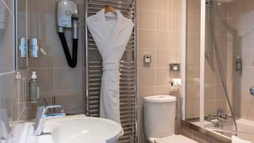 Un baño moderno con lavamanos, inodoro y ducha blancos. Un albornoz blanco cuelga en un perchero, y hay artículos de aseo en la encimera.