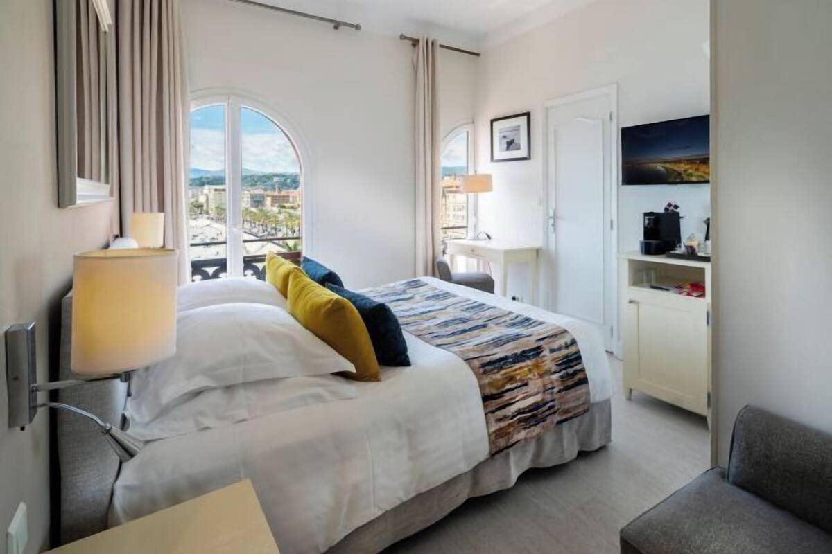A hotel room with a bed, a desk, a chair, a TV, and a view of the city.