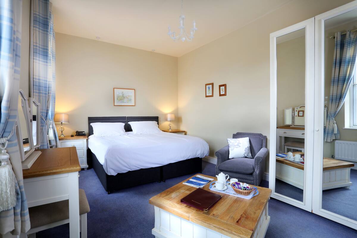 A hotel room with a bed, a desk, a chair, a coffee table, and a mirror.