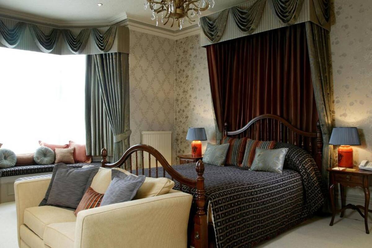 A bedroom with a large bed, two bedside tables with lamps, a sofa, and a window with curtains.