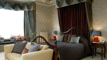 A bedroom with a large bed, two bedside tables with lamps, a sofa, and a window with curtains.