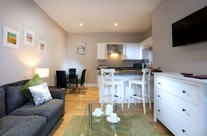 Una sala de estar moderna con un sofá gris, una mesa de centro de vidrio y un mueble blanco.