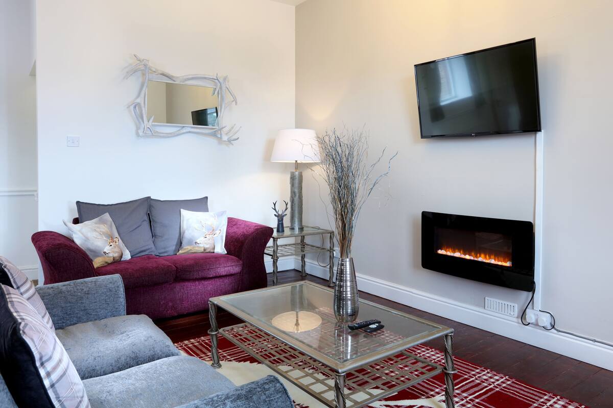A living room with a red and grey sofa, a glass coffee table, a fireplace, and a mounted TV.