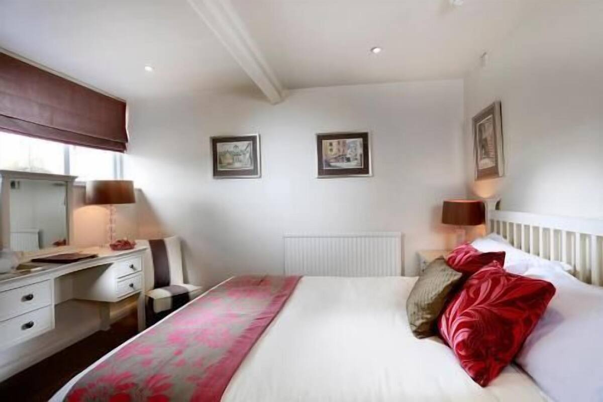 A bedroom with a bed, bedside tables, a dresser, a radiator, and two framed pictures on the wall.