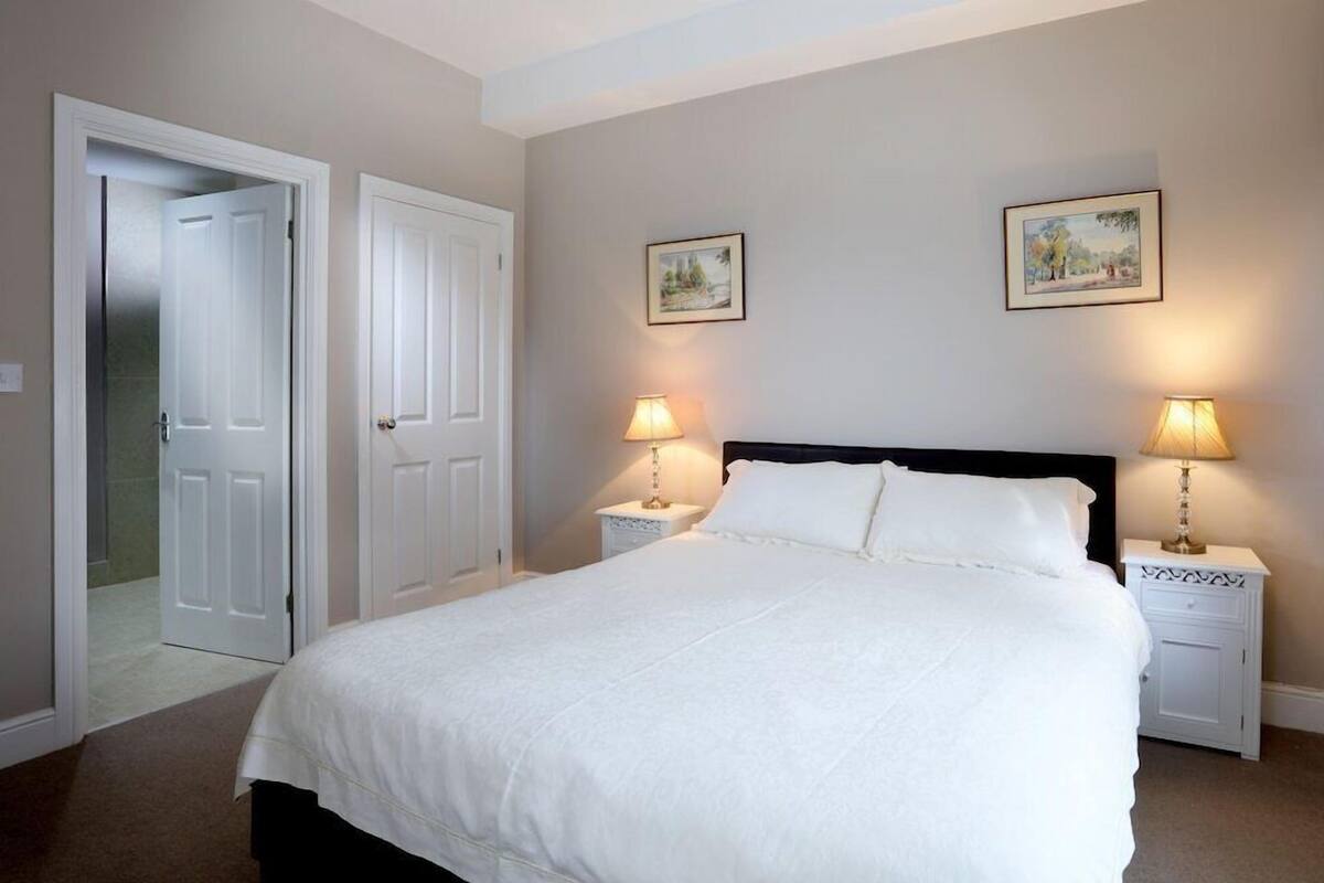 A bedroom with a bed, two bedside tables, two lamps, and two framed pictures on the wall.