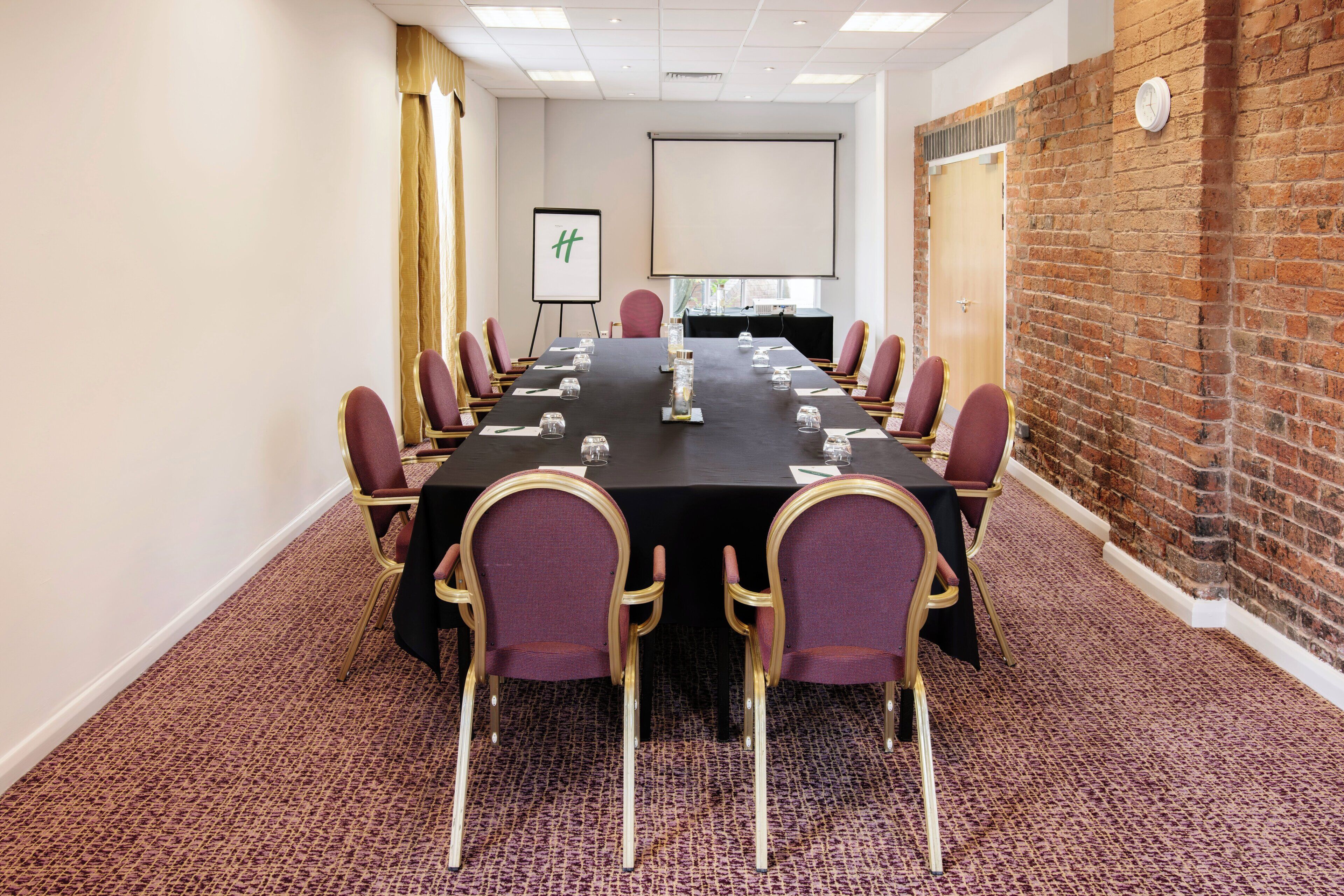 A conference room with a long table, chairs, a projector screen, and a brick wall.