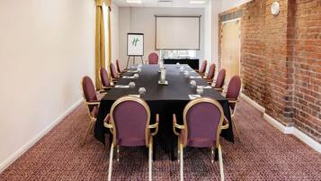 A conference room with a long table, chairs, a projector screen, and a brick wall.