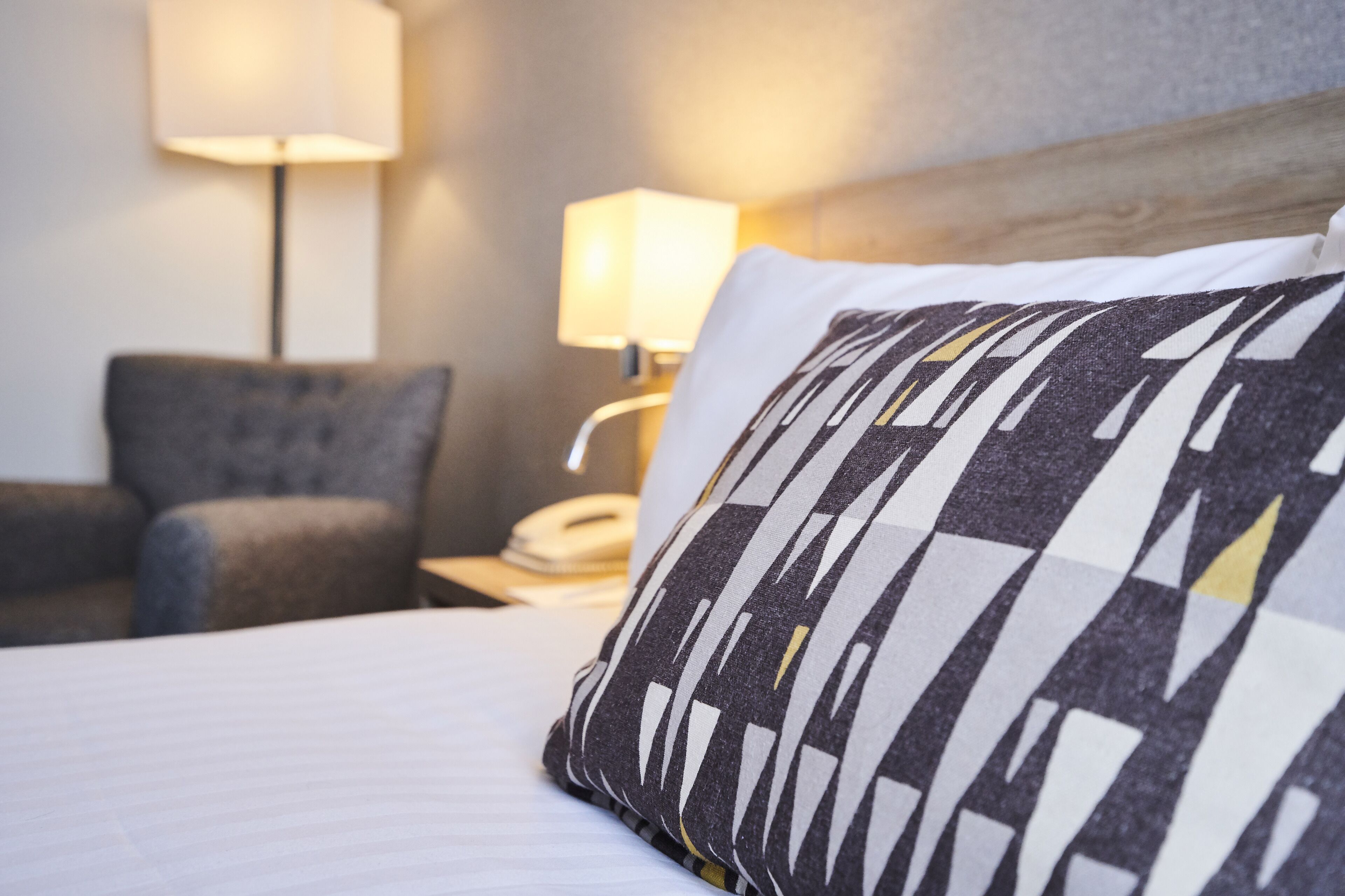 Una habitación de hotel con cama, mesita de noche con lámpara y una silla.