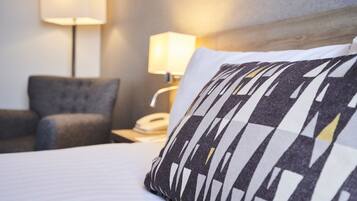 Una habitación de hotel con cama, mesita de noche con lámpara y una silla.