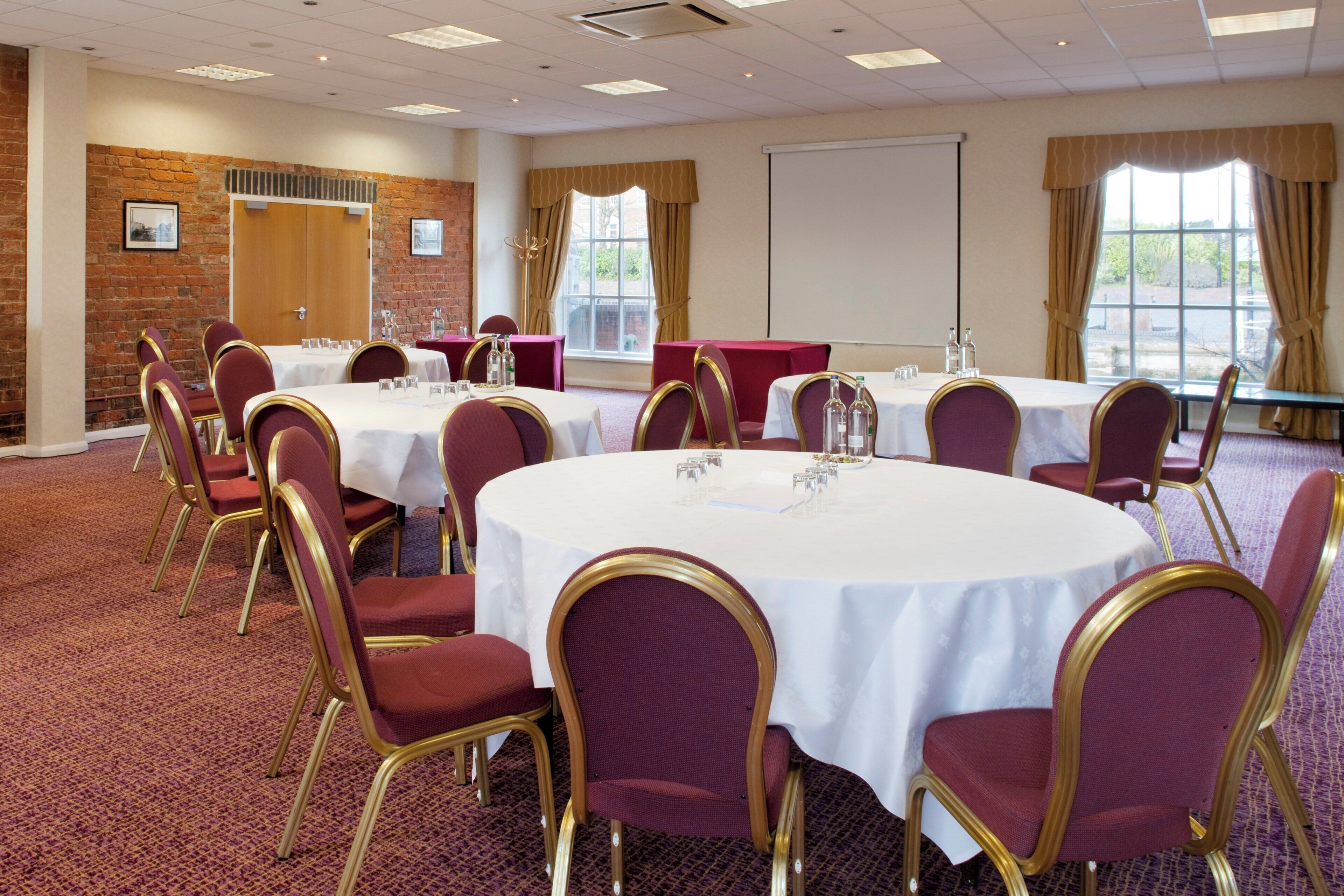 A conference room with round tables, chairs, and a projector screen.