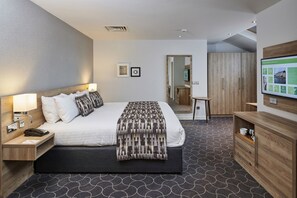 A modern hotel room with a large bed, bedside tables, a desk, and a wardrobe.