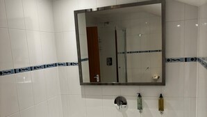 A modern bathroom with a large bathtub, a mirror above it, and two bottles of soap on the wall.