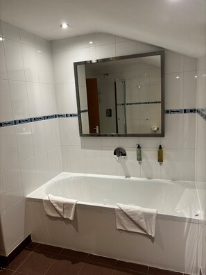 A modern bathroom with a large bathtub, a mirror above it, and two bottles of soap on the wall.