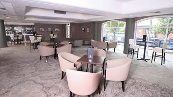En hotelllobby med sittgrupper, en bardel och stora fönster som ger utsikt över omgivningen.