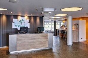 Un hall d’hôtel moderne comprenant un comptoir d’accueil, un espace repas et un bar.