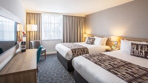 A hotel room with two beds, a desk, a chair, and a TV.